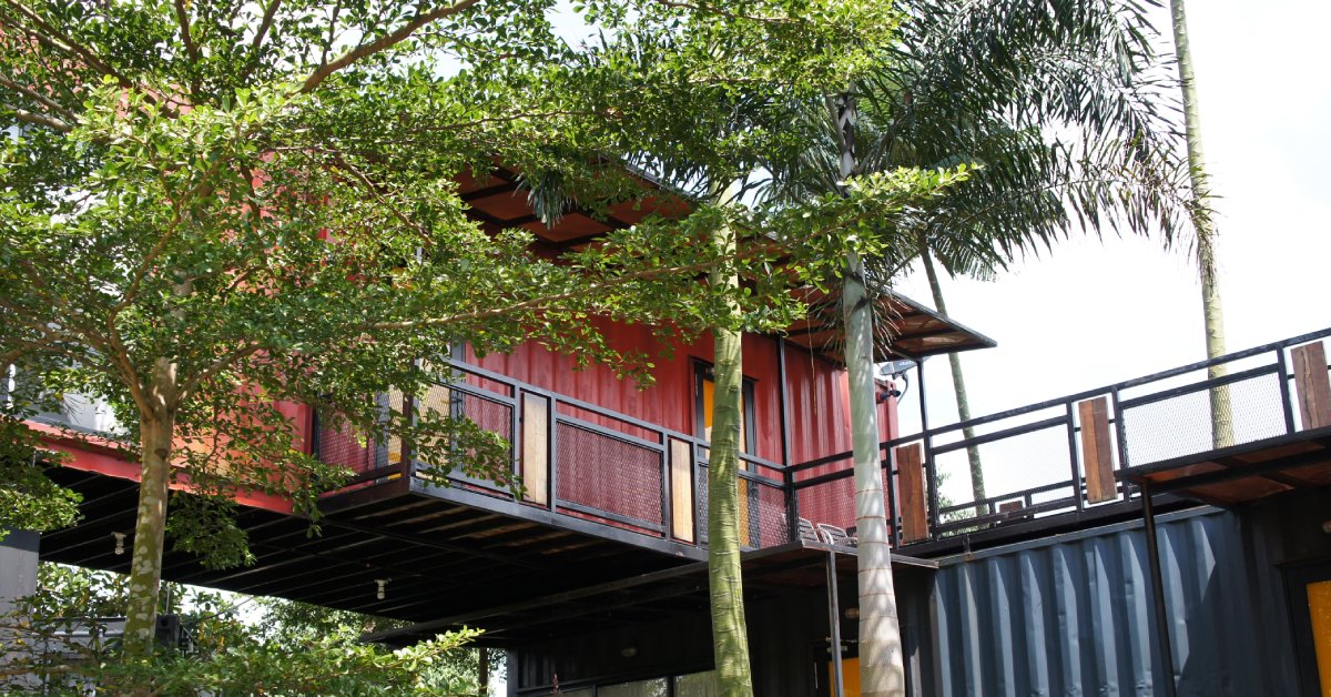 Three flourishing trees stand in front of an environmentally-friendly two-story building made from shipping containers.
