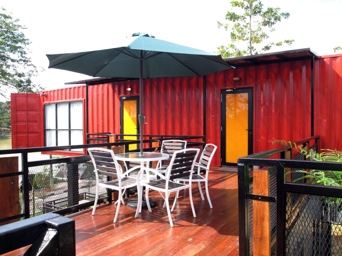 A table with an umbrella sits on the deck in front of a trendy building made from a refurbished shipping container.