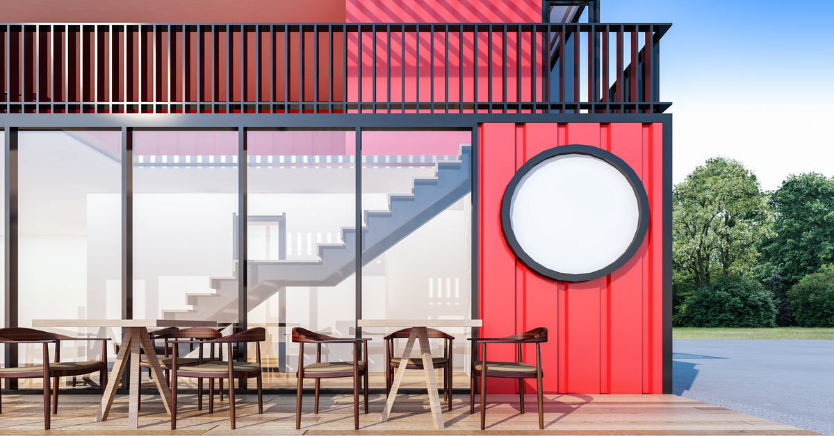 A red shipping container business space has a patio area and large windows. Stairs are visible inside.