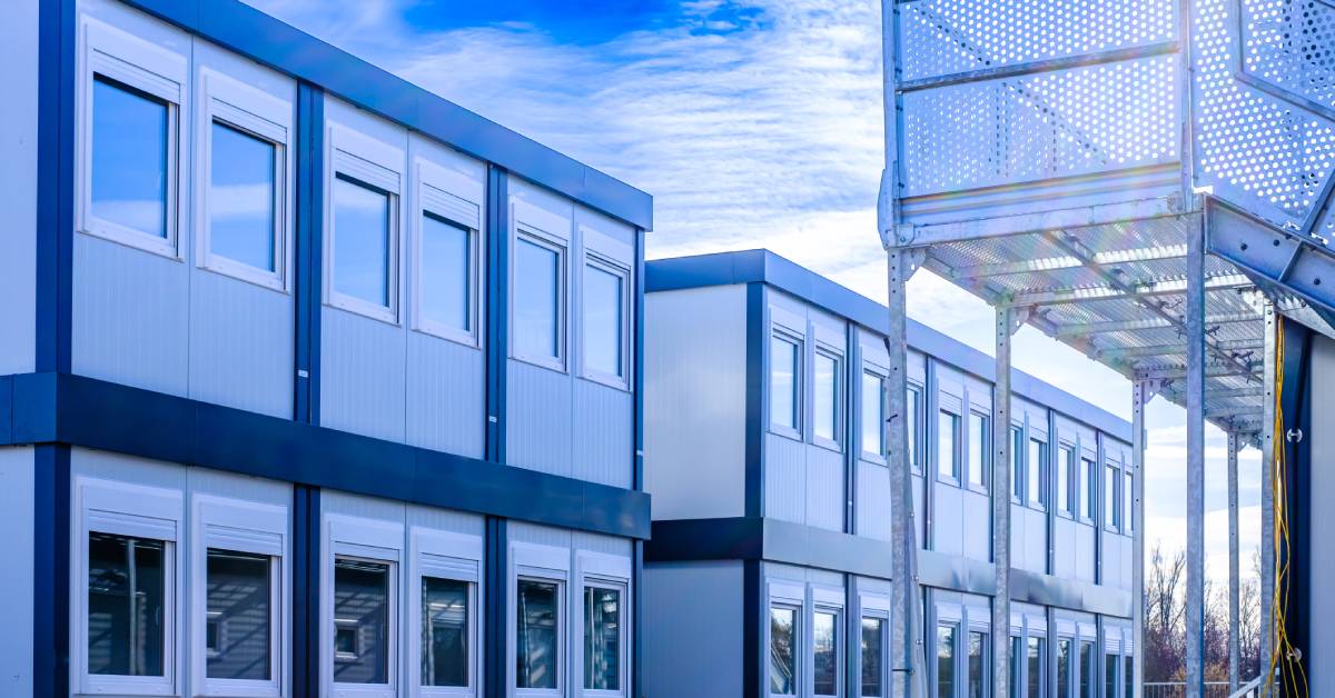 A complex of two story shipping container buildings with windows. There is a staircase nearby and a blue sky above.