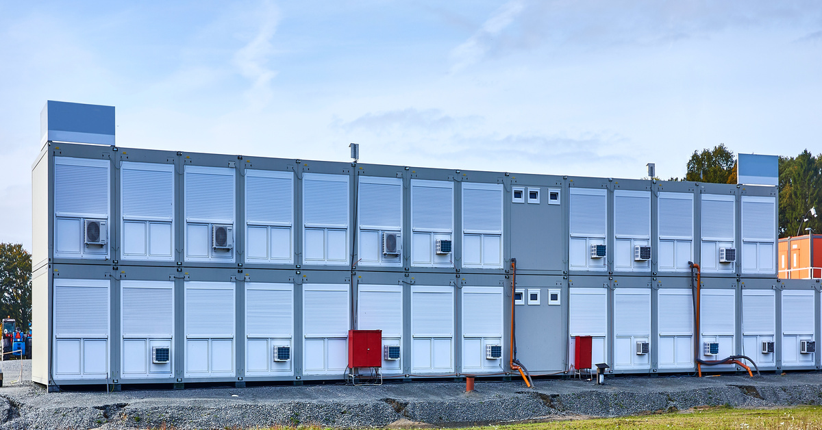 A structure made out of stacked shipping containers in a complex area. There are window air units on each one.